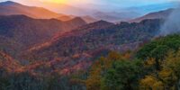 At sunset in the Blue Ridge Mountains, the sun light escapes under an overhead cloud bank to illuminate ridges and autumn valleys in its warm glow. North Carolina along the Blue Ridge Parkway.